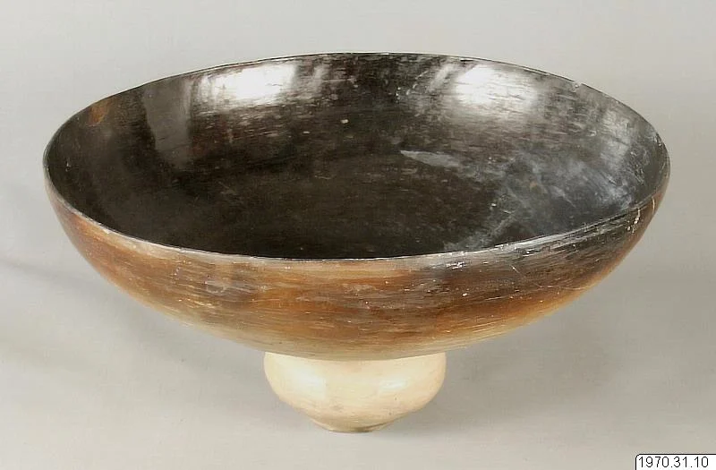 A shallow rounded ceramic vessel with a dark interior, brown outer wall and pale rounded foot, shown complete with its inventory number.