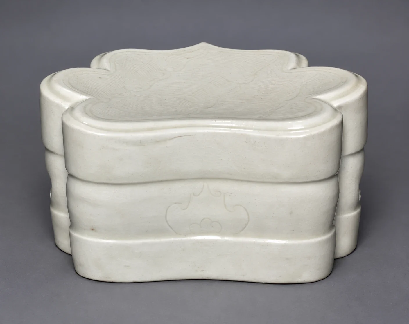Pale cloud-shaped porcelain pillow with incised waves.