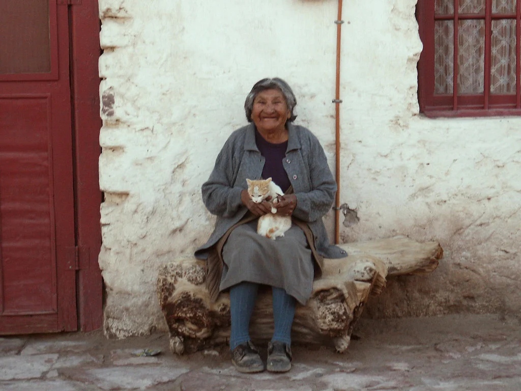 A woman identified by photographer Jose Manuel Podlech as Aymara, seated with a cat in Chiu Chiu, Chile, in 2004
