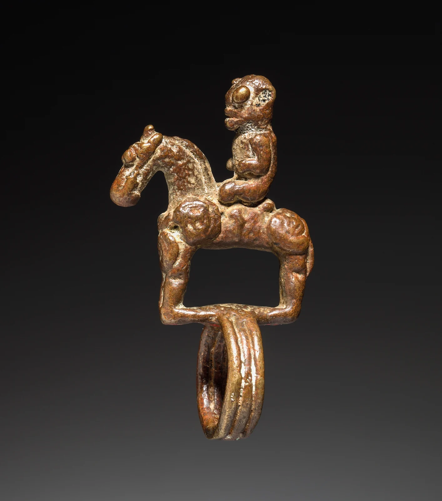 Copper-alloy ring with a small rider on a bridled horse above the ring band, photographed against a dark background.