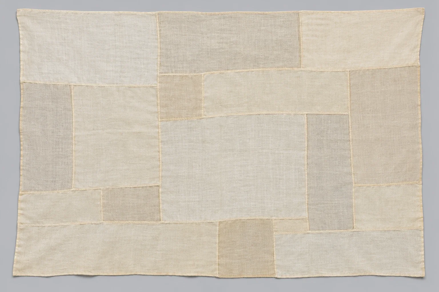 AI-generated illustration: One flat pale cloth assembled from irregular rectangular fabric patches, with fine sealed-looking seams forming a window-pane network.