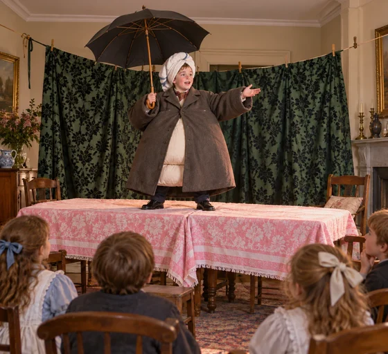 Imagined Jimmy in a pillow-padded overcoat and towel stage turban holds an umbrella on a homemade stage.