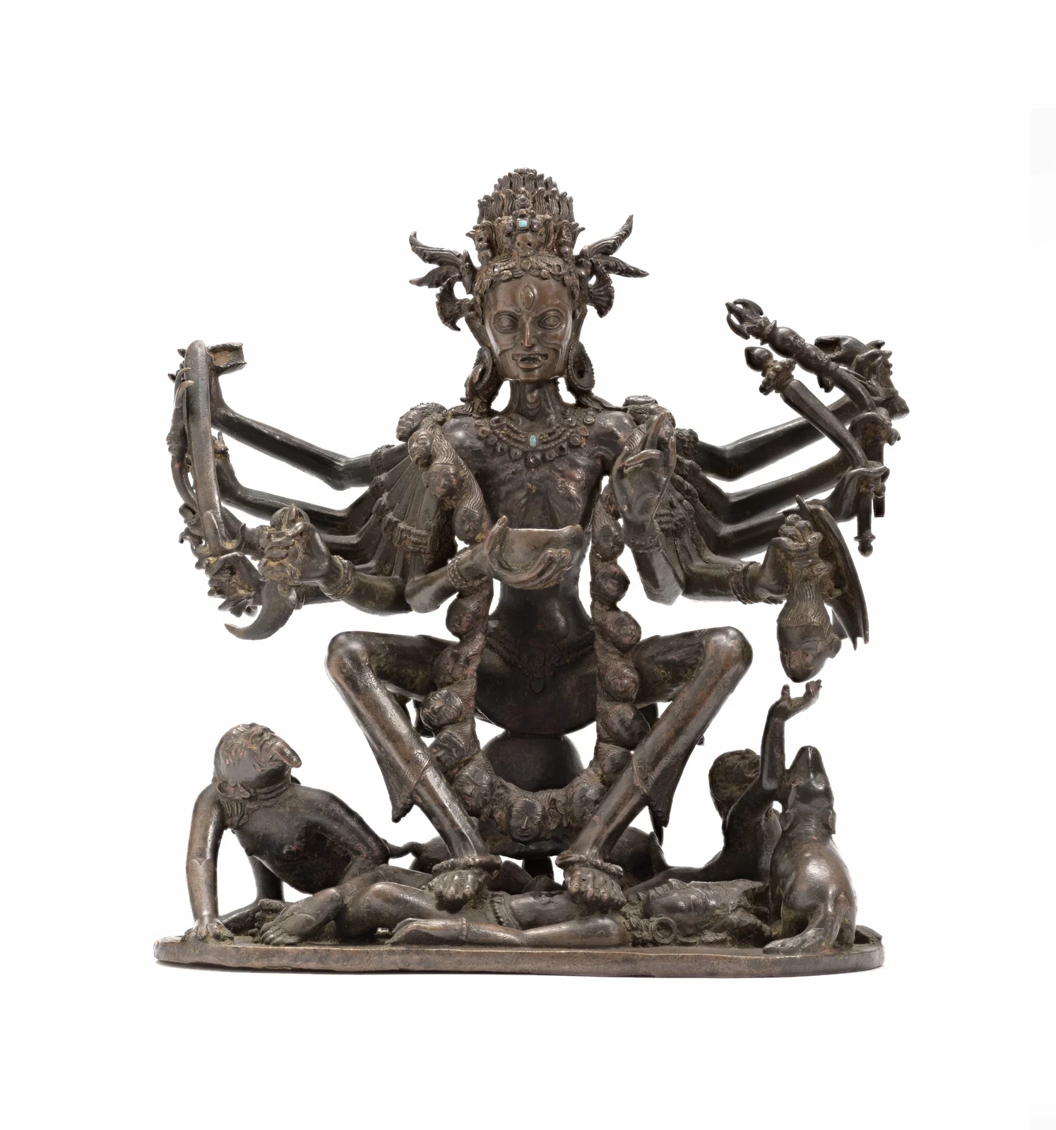 Copper sculpture of many-armed Chamunda above a reclining corpse, flanked near the base by two small humanlike ghouls; a jackal also sits at the right.
