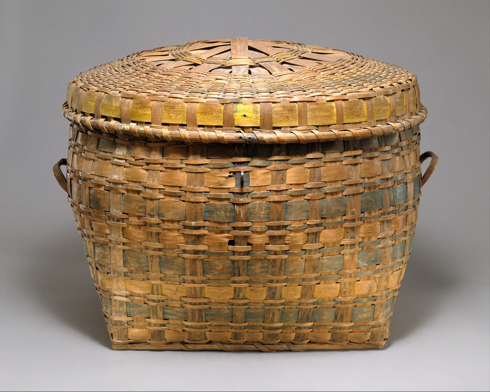 Oval lidded woven basket with faded green and yellow bands and two side handles; attributed uncertainly to Passamaquoddy makers, circa1840.