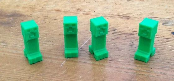 Four small green 3D-printed Creeper figures with square heads and recessed pixel faces, standing on a wooden tabletop.