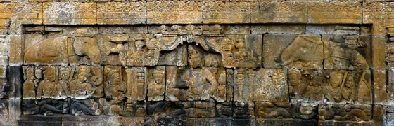 Long stone relief of a seated royal figure beneath a central pavilion, with a halo behind his head and courtly figures seated on either side.