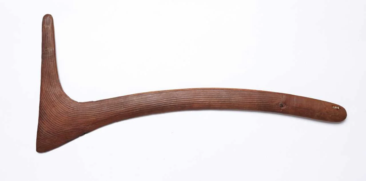 A complete angular wooden boomerang with closely carved grooves on a white background.