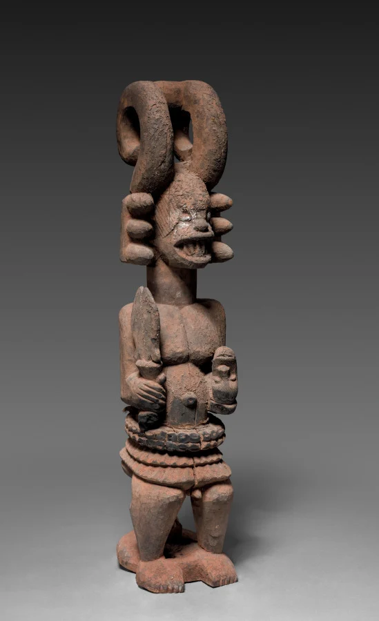 Wooden ikenga shrine figure with curved horns, photographed against a grey background.