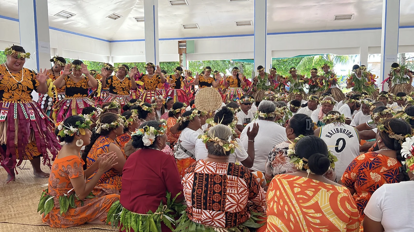 Standing and seated performers in an open hall, wearing colourful patterned clothing and leaf garlands; the photographer identifies this as a Nanumea group performing fatele in Funafuti.