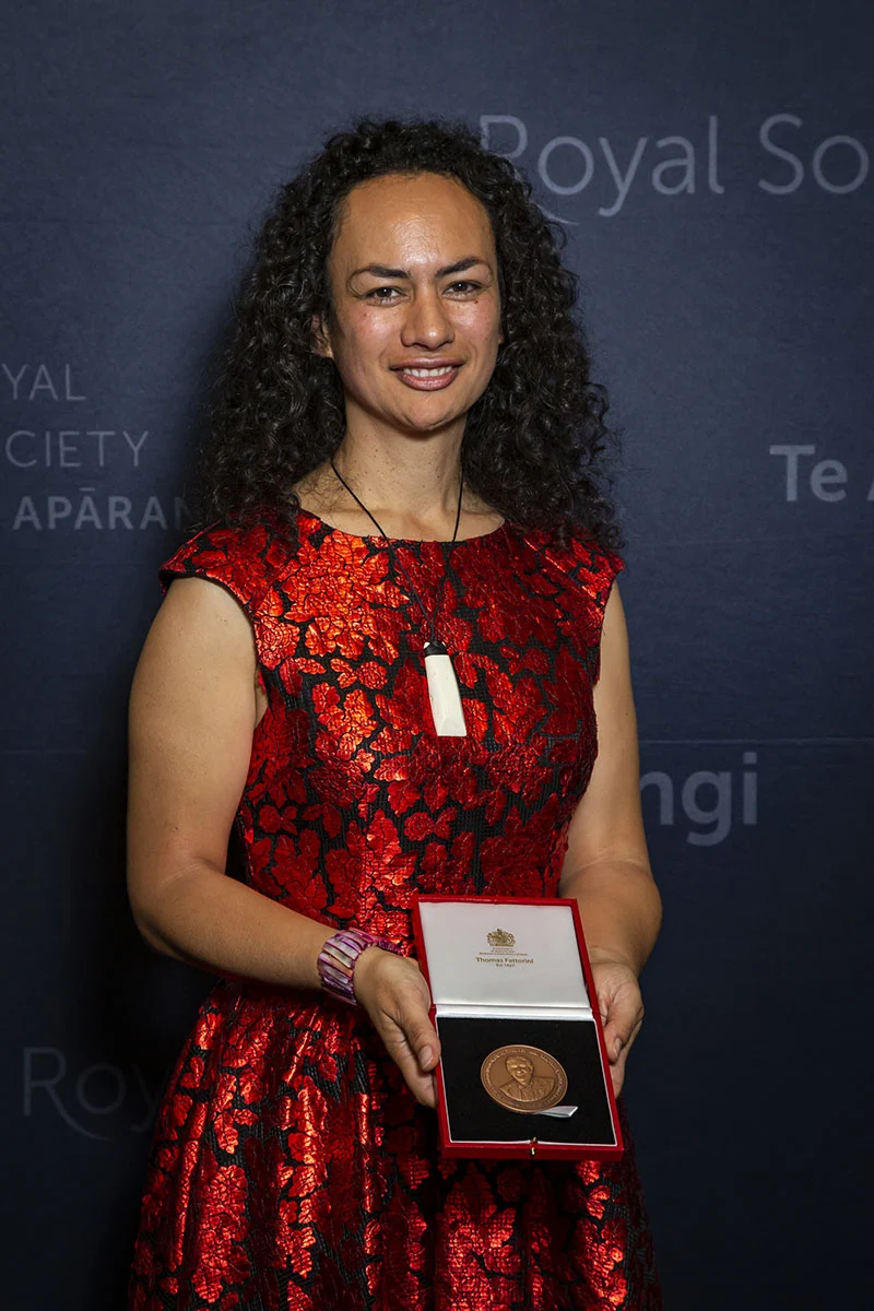 Ocean Mercier, identified by Royal Society Te Apārangi as Ngāti Porou, holds an open medal case at its 2019 Research Honours Aotearoa ceremony, wearing a red-and-black dress.