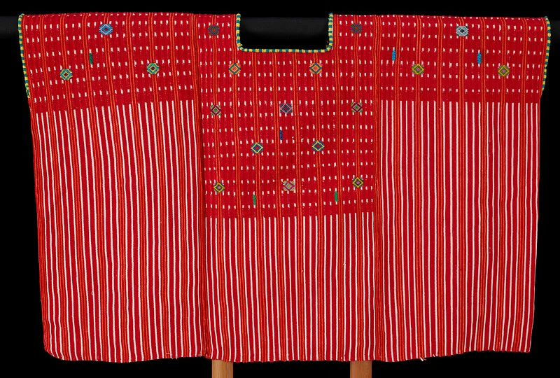 A red Mam Maya blouse displayed flat against black, with white vertical stripes, small multicoloured diamond motifs and a rectangular neckline edged in yellow and green.