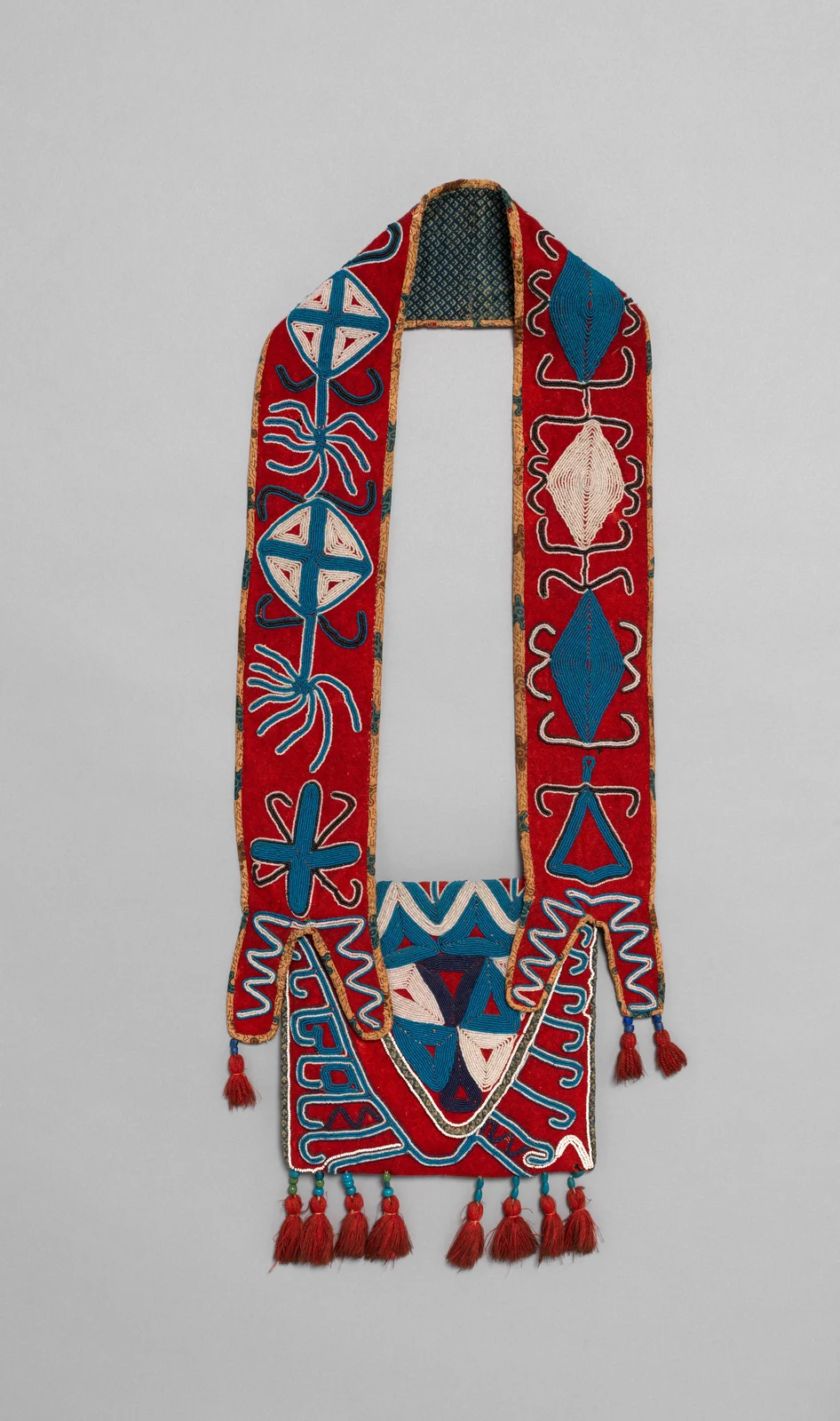 Red shoulder bag with a broad asymmetrically patterned strap, blue and white beadwork and red tassels; Seminole, Florida, circa1830.
